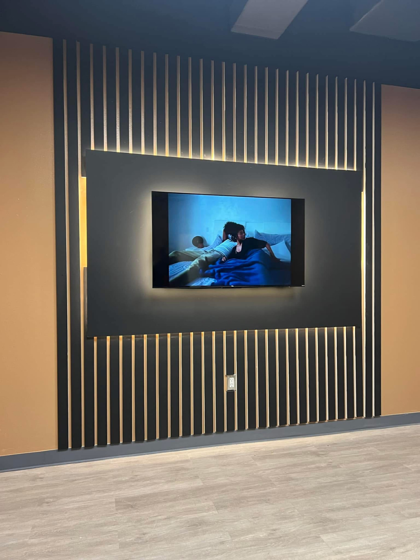 Dark accent wall with backlit wood slats and a flush-mounted TV